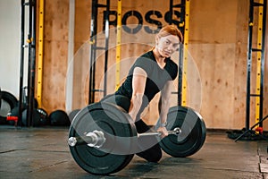 Leaning on the barbell. On the floor. Beautiful strong woman is in the gym