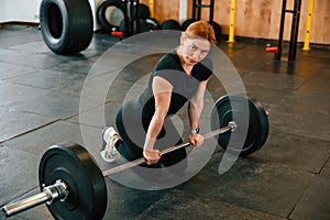 Leaning on the barbell. On the floor. Beautiful strong woman is in the gym