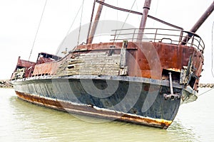 Leaning broken and rusty shipwreck marooned in cove near shore,