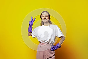 Ð¡leaning concept. Young woman in blue glowes on bright yellow studio wall background