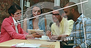 Leaning in four coworkers collaborating around meeting room table, with tablet and notepad