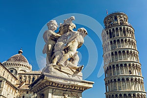 The leaning tower of pisa and cathedral at daytime. Statue with angels in the foreground.