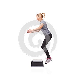 Leaping up in pursuit of fitness. A smiling young woman doing aerobics on an aerobic step against a white background.