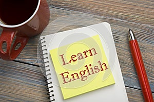 Learn English Text written on notebook page, red pencil and coffee cup. Office desk table top view