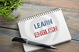 Learn English Text written on notebook page, red pencil and coffee cup. Office desk table top view