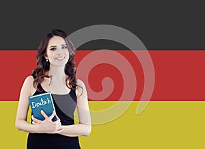 Learn German language. Attractive young woman holding phrasebook against the Germany flag background