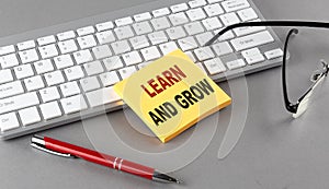 LEARN AND GROW text on a sticky with keyboard, pen glasses on grey background