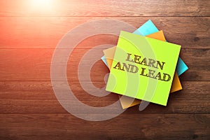 Learn and Lead, the phrase is written on multi-colored stickers, on a brown wooden background. Business concept, strategy, plan,