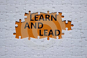 Learn and lead symbol. Concept words Learn and lead on white puzzle. Beautiful orange background. Business and Learn and lead