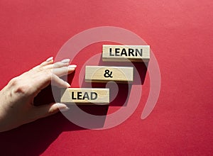 Learn and lead symbol. Concept words Learn and lead on wooden blocks. Beautiful red background. Businessman hand. Business and