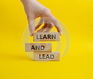 Learn and lead symbol. Concept words Learn and lead on wooden blocks. Beautiful yellow background. Businessman hand. Business