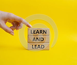 Learn and lead symbol. Concept words Learn and lead on wooden blocks. Beautiful yellow background. Businessman hand. Business