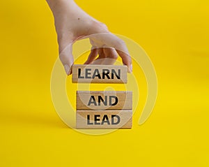 Learn and lead symbol. Concept words Learn and lead on wooden blocks. Beautiful yellow background. Businessman hand. Business