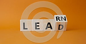 Learn and Lead symbol. Turned wooden cubes with words Learn and Lead. Beautiful orange background. Business and Learn and Lead