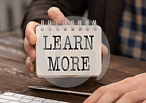 Learn More text written on a notebook in hand, business concept.
