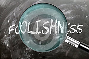 Learn, study and inspect Foolishness. A magnifying glass enlarging word \'foolishness\' written on a blackboard photo