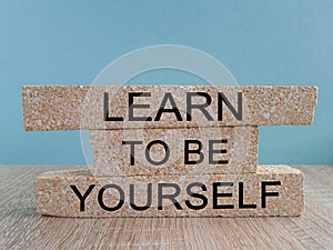 Learn to be yourself symbol. Brick blocks with words Learn to be yourself on beautiful blue background.