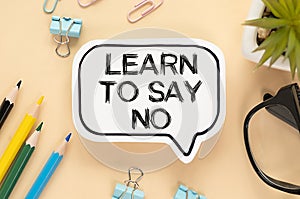 LEARN TO SAY NO written in a white notebook on a light wooden background near a calculator, a cup of coffee, glasses and a pen.