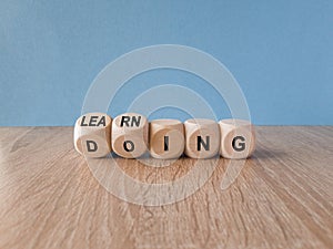 Learning by doing concept. Turned a cube and changes the word learning to doing, or vice versa. Beautiful wooden table blue