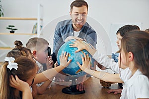 Learning geography by using Earth globe. Group of children students in class at school with teacher