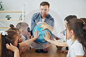 Learning geography by using Earth globe. Group of children students in class at school with teacher