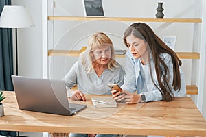 Learning how to use modern technologies. Smartphone and laptop. Mother and daughter is together at home