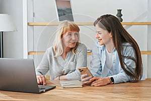 Learning how to use modern technologies. Smartphone and laptop. Mother and daughter is together at home