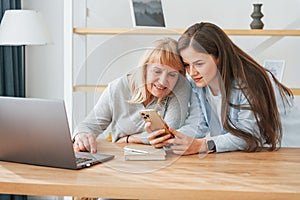 Learning how to use modern technologies. Smartphone and laptop. Mother and daughter is together at home