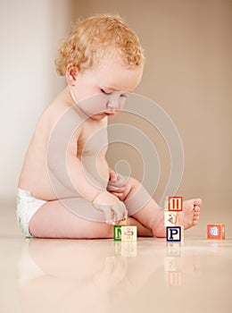 Learning through interactions. Cute little baby sitting on the ground and playing with some alphabet blocks.