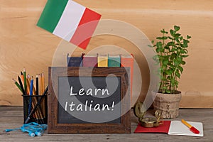 Learning languages concept - blackboard with text "Learn italian!", flag of the Italy, books, chancellery