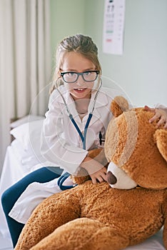 Learning medicine from a young age. a little girl pretending to be a doctor while examining her teddybear.