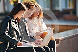 Learning, sitting and using laptop. Three young students are outside the university outdoors