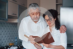 Learning some new stuff. Man and his wife in white shirt preparing food on the kitchen using vegetables
