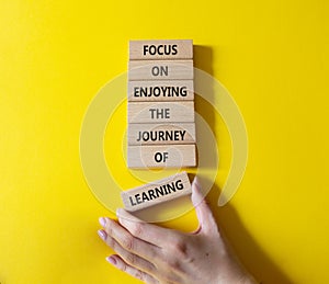 Learning symbol. Wooden blocks with words Focus on enjoying the journey of learning. Businessman hand. Beautiful yellow background