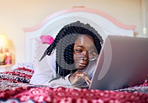 Learning about technology. an adorable little girl using a laptop while lying on her bed in her bedroom.