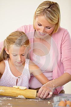 Learning to bake - Perfecting her technique. A mother helping her daughter to rollout the cookie dough.
