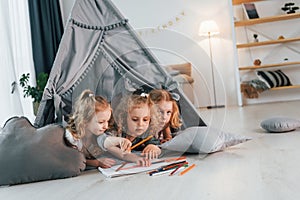 Learning to draw. Girls is laying down in the tent. Group of children is together at home at daytime