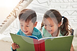 Learning to read together. two adorable young siblings reading a book together at home.