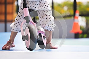 Learning to ride a bike concept, little kid girl is practicing her balance by riding plow bike on training slope for little ones.