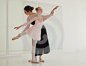 Learning a valued art form. a young girl practicing ballet with her teacher in a dance studio.