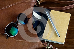 Leather Bag with Passport Sunglasses Pen and Notebook on a Polished Wooden Surface