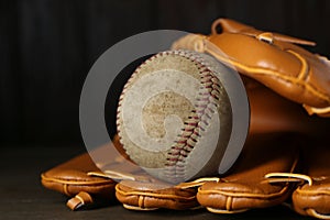 Leather baseball glove with old worn ball on wooden table, closeup