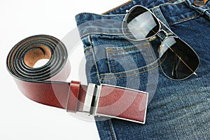 Leather belts, jeans, sunglasses on white background