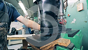 Leather boot is getting put into its sole by a factory worker. Worker sewing shoes. Footwear factory facility.