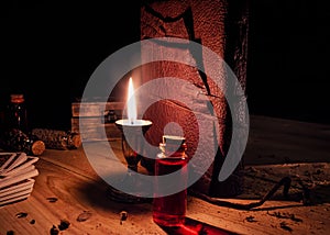 Leather bound tome, a candle and a potion on a wooden surface