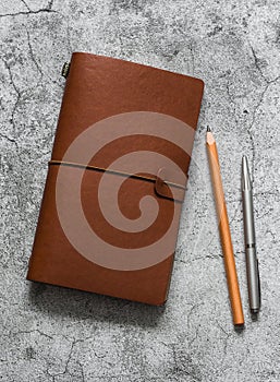 Leather brown personal organizer, pen, pencil  on a gray table, top view. Business concept, copy space