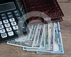 Leather brown wallet, dollars and a calculator on a wooden background.