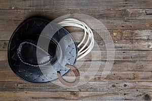 Leather cowboy hat with lasso and horseshoe on rough wooden table