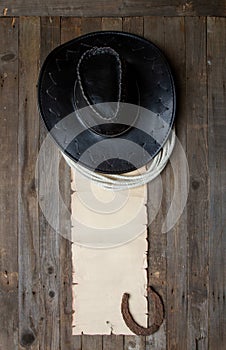leather cowboy hat with lasso and horseshoe on rough wooden table and blank paper with place for text