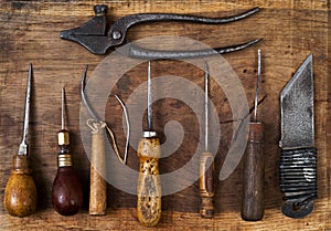 Leather craft tools on a wooden background. Craftmans work desk. Piece hide and working handmade tools. Top view.